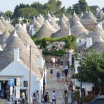 Trulli pugliesi circondati da fiori primaverili e mare cristallino in un itinerario di marzo.